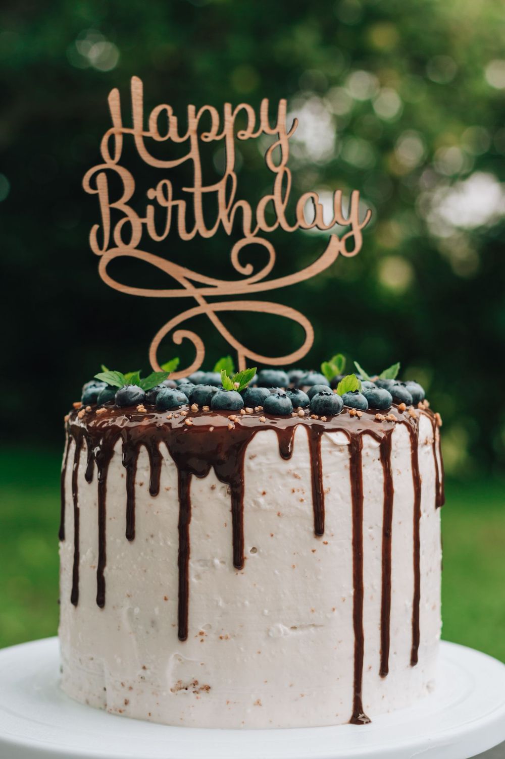 Cake Topper aus Holz mit dem Schriftzug „Happy Birthday“ in Schreibschrift auf einer Torte mit Heidelbeeren